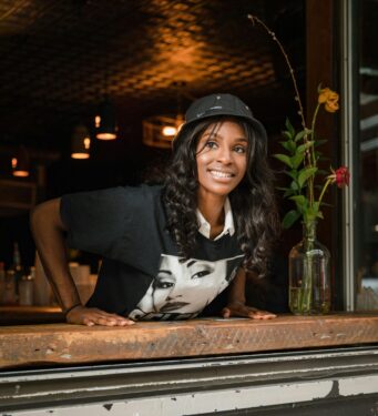 Businesswoman smiling behind a bar counter at a black-owned business promoting community support.